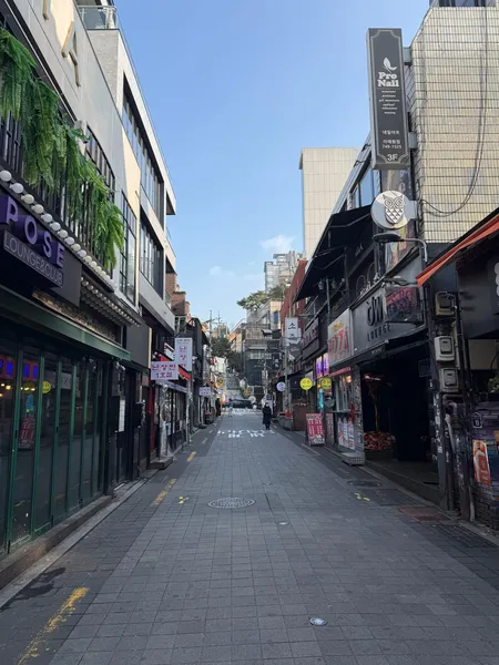 A side street in Itaewon, Seoul, lined with bars and signage under a clear sky.